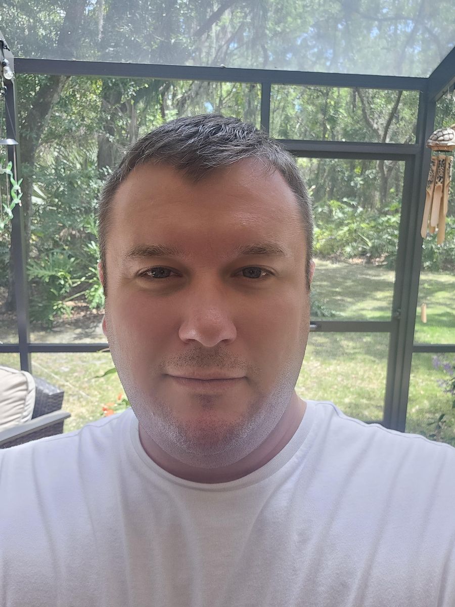 Sean Henne smiling, standing on a screened porch with trees behind him